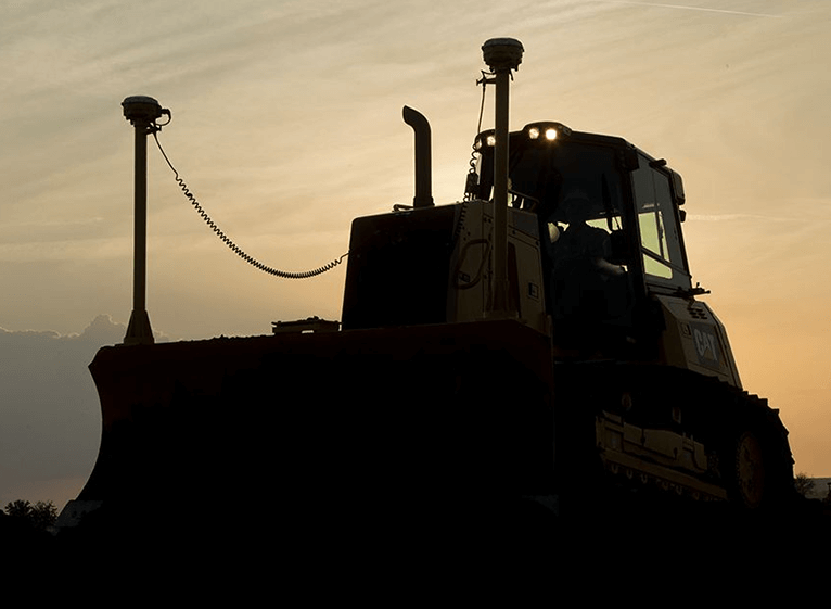 Μπουλντόζα Caterpillar σε silhouette στο ηλιοβασίλεμα, με GPS κεραίες στο εμπρόσθιο τμήμα και τεχνολογία μηδενικής εκπομπής.